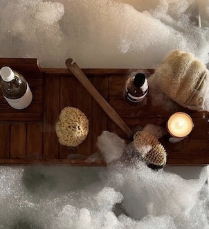 image shows an overhead view of a bathtub, wooden tray and bath products, including bath oils, loofah and candles.